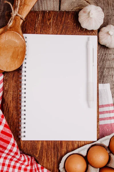 Tahta kesme tahtasıyla sarımsak, kepçe, yumurta ve boş bir defter.