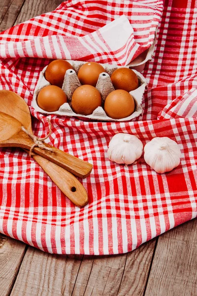 Tahta kepçe, sarımsak ve yumurta kırmızı ve beyaz bir masa halısı üzerinde.