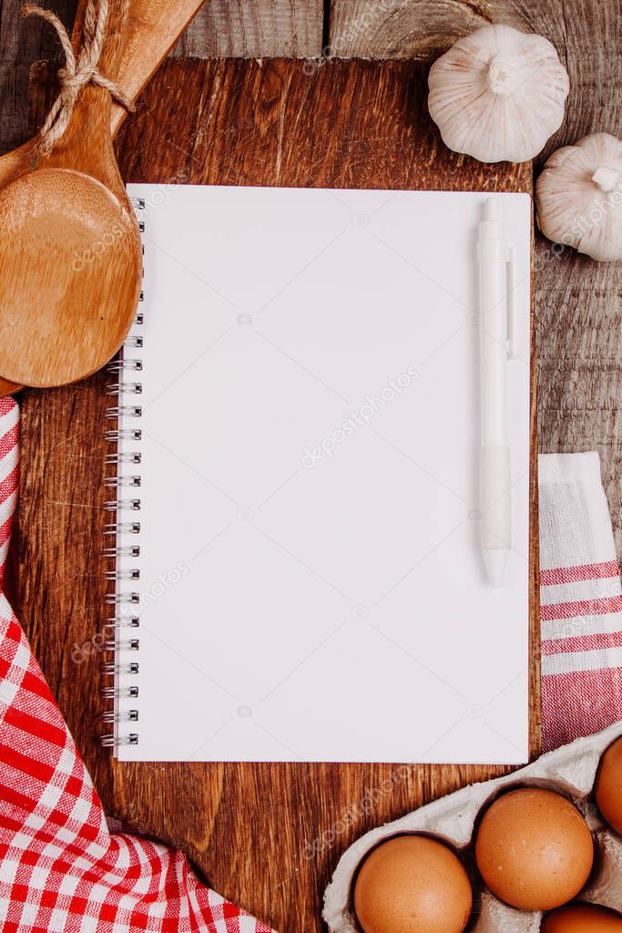 Wooden cutting board on a wooden background with garlic, ladles, eggs and a blank notebook