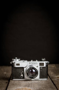 Ahşap bir masanın üzerinde siyah arka planı olan eski model bir fotoğraf makinesi.