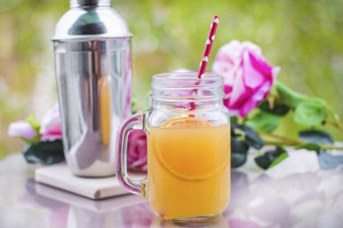Cam bir kavanozda portakal suyu kokteyli, güller ve bir karıştırıcı.