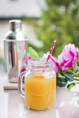 Cam bir kavanozda portakal suyu kokteyli, güller ve bir karıştırıcı.