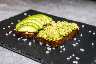 Kahvaltıda siyah tabakta sağlıklı avokado tostu.