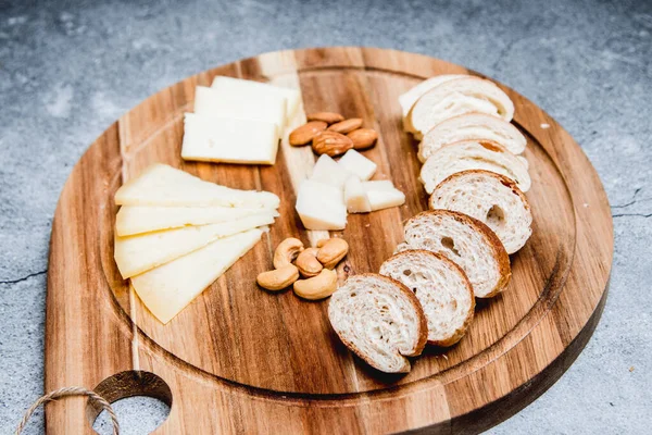 Tahta tabakta kahvaltı için peynir, fındık ve küçük ekmek.