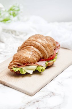 Tahta bir masa ve mermer bir yüzey üzerinde sandviç kruvasanı.
