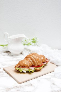 Tahta bir masa ve mermer bir yüzey üzerinde sandviç kruvasanı.
