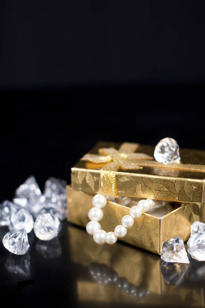 Golden jewellery box with shiny pearls on a black glossy background