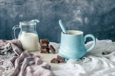 Pastel mavi kahve fincanı, bir şişe süt ve çikolata kırsal masada ve arka planda.