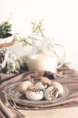 Beyaz ahşap bir masada tüyleri ve bahar çiçekleri olan güzel pastel yumurtalar.