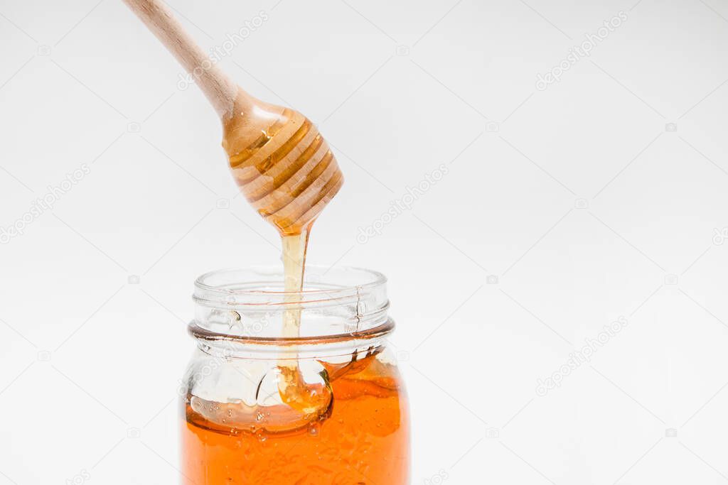 A close up of a decorative honey jar and a honey spoon on a white background