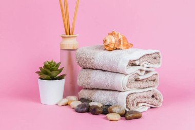 Spa malzemeleri, aroma çubukları taşlar, havlular ve pembe arka planda bir bitki.