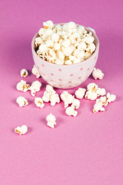 Pembe ve mavi arka planda beyaz bir kasede taze patlamış mısır.