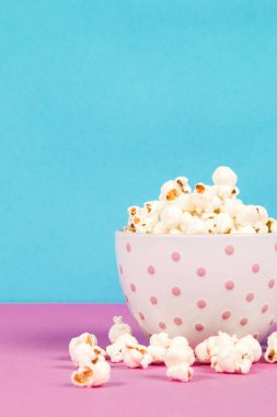 Pembe ve mavi arka planda beyaz bir kasede taze patlamış mısır.