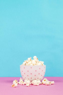 Pembe ve mavi arka planda beyaz bir kasede taze patlamış mısır.