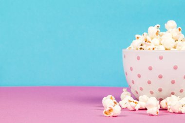 Pembe ve mavi arka planda beyaz bir kasede taze patlamış mısır.