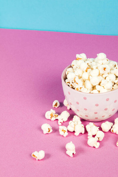 Fresh popcorn in a white pink bowl on pink and blue background