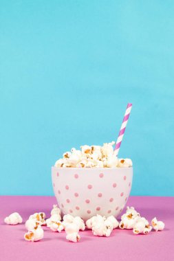 Pembe ve mavi arka planda beyaz bir kasede taze patlamış mısır.