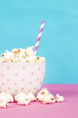 Pembe ve mavi arka planda beyaz bir kasede taze patlamış mısır.