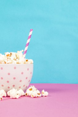 Pembe ve mavi arka planda beyaz bir kasede taze patlamış mısır.