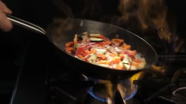 La persona scuote le verdure tagliate sulla padella sopra la fiamma aperta — Video Stock