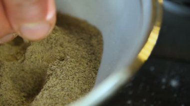 Makro pişirme parmakları baharatlara dokunur. Mutfak masasındaki beyaz kasede, parlak ışık arka planında.