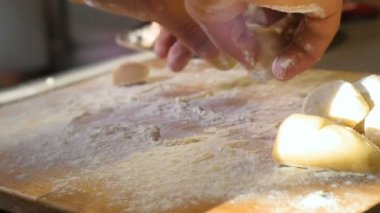 Kapalı makro eller parlak gün ışığına karşı tahtanın üzerinde un ile hamur çemberleri oluşturur.
