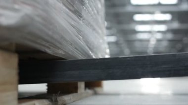 Kargo makinesinin metal çatalı ahşap tepsiyi büyük bir depoda kalın beyaz polietilen plastik film ile kaldırır ve yükler.