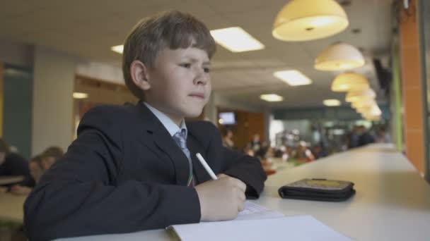 Schooljongen schrijven in notitieblok aan kantine tafel — Stockvideo