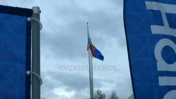 Banderas en postes ondeando en el viento cerca de edificios — Vídeos de Stock