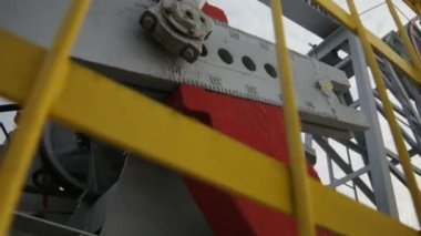 Yakından çekilen kamera büyük kırmızı ve gri çelikten ağırlık arkaplanda gri bulutlu gökyüzünü gösteriyor.