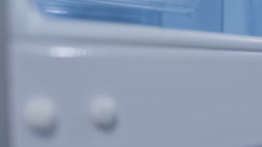 Yumuşak odaklı yakın çekim kamerası beyaz, açık buzdolabı köşesi ve raflar boyunca yavaşça hareket eder.