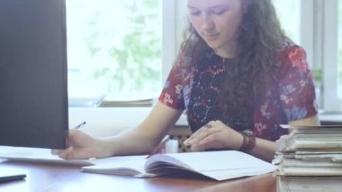 Kazan, Tataristan/Rusya - 12 Haziran 2016: Kıvırcık saçlı güzel genç kız masa başında oturan belgelerle çalışır bilgisayar üzerinde 12 Haziran kazan karşısında