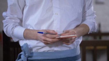 Beyaz resmi bluzlu, kalem ve turuncu defterli garson restoranda siparişi bekliyor.