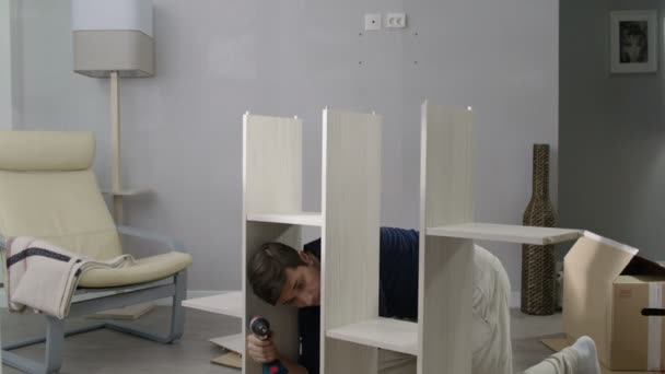 Handsome Guy Assembles New Bookcase Drill Wooden Parquet Grey Walls — ストック動画