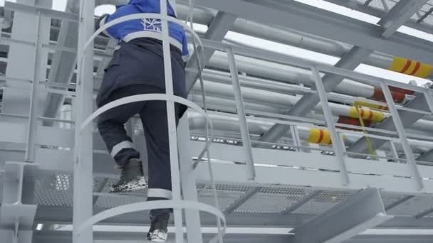 Работник нефтяной компании взбирается по лестнице — стоковое видео