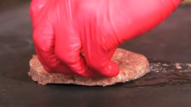 portre yan görünüm yuvarlak çiğ et pirzola kızgın yağda siyah fırın tepsisinde koymak kırmızı eldiven eller