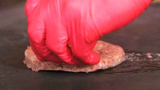 黒天板に熱い油でラウンド原料肉のカツを入れて赤い手袋で手をクローズ アップ側ビュー — ストック動画