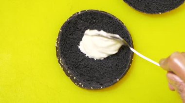 closeup üst görünüm Ocak beyaz sos siyah burger çörek kaşıkla koyar ve sarı tablo döndürür