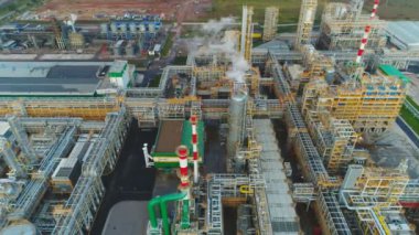 İnsansız hava aracı, metal yapılar ve duman yayan modern ekipmanlarla büyük rafineri bölgesinin üzerinde uçuyor.