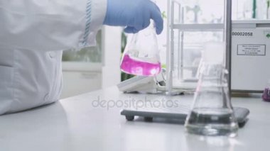 closeup yetenekli kimyager kıyafeti sıvı cam içinde sallar ve pembe kimyasal saydam olur