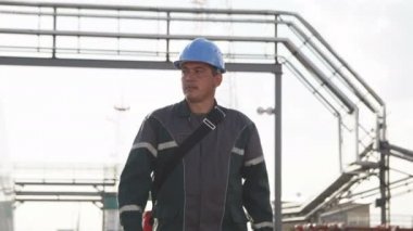 Kazan, Tataristan/Rusya - 04 Eylül 2017: Genç bir mühendis yürür ve modern gaz rafineri tesisi alanı ile boru hatları ve beyaz tank üzerinde 04 Eylül kazan üzerinde etrafına bakıyor