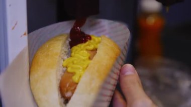Kadın fast food kafede sosisli sandviçe ketçap ekliyor.