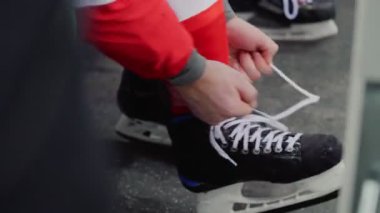 Hokey oyuncusu kaykayını bağlıyor, bankta oturuyor.