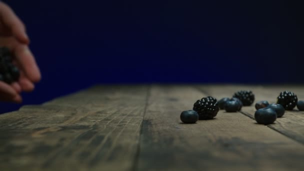 Person wirft saftige Beeren auf rustikalen Tisch Zeitlupe — Stockvideo