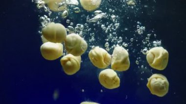 ravioli falls down into clear hot water on blue background