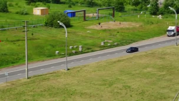 Black automobile drives along road past lush meadow aerial — Stock Video