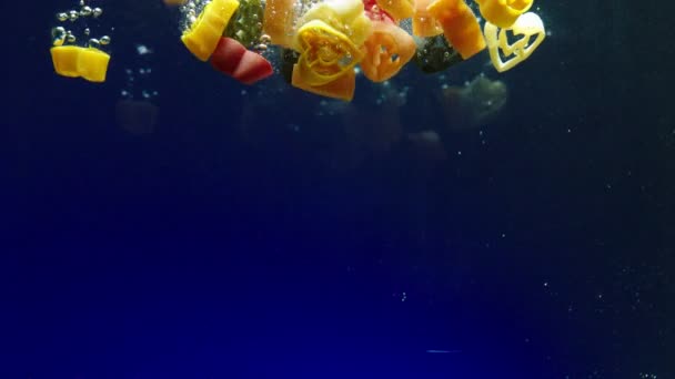 Pasta multicolor cae en el agua primer plano cámara lenta — Vídeos de Stock