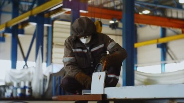 Worker grinds metal detail with tool on floor in workshop — ストック動画