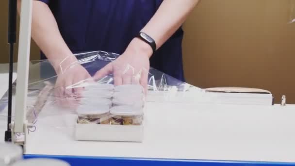 Employee packs box of jars with foil at table in workshop — Stock Video