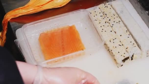 Man zet zalm vis op sushi roll aan tafel close view — Stockvideo